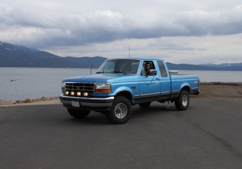 1992 Ford F-150 - A blue 1992 Ford F-150 pickup truck is parked near a body of water under a cloudy sky.