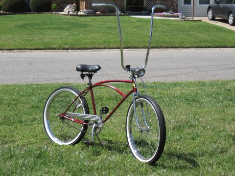 1994 Ford Bronco - A custom cruiser bicycle with a red frame and high handlebars sits on a grassy lawn in front of a suburban house.