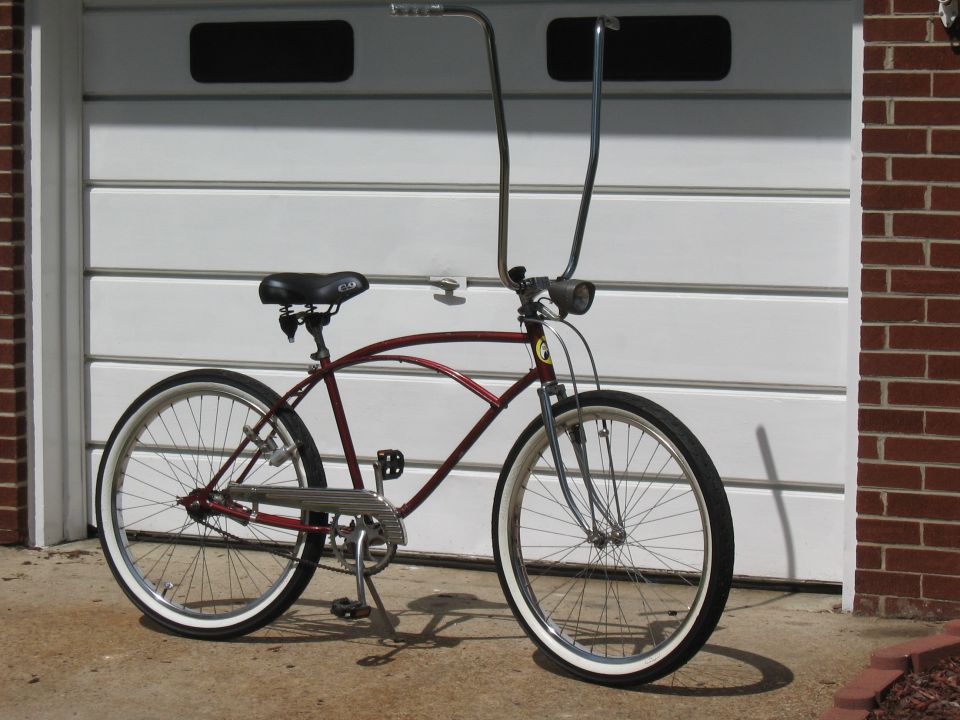 Maroon cruiser bicycle with tall handlebars and whitewall tires parked in front of a garage door