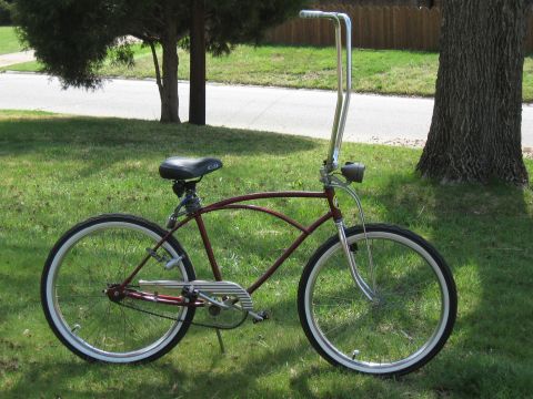 1994 Ford Bronco - Cruiser bicycle with tall handlebars and whitewall tires parked on grass next to a tree.