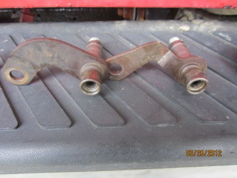1979 Ford Bronco - Two metal linkage arms, likely for a transmission, are shown resting on a textured surface.