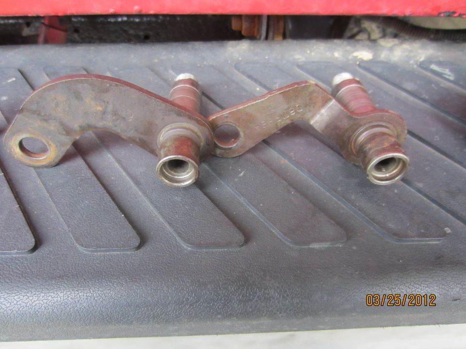 Two rusty metal transmission linkage arms with pins on a black textured surface