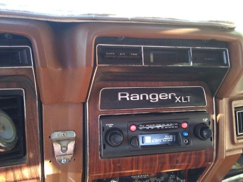 1981 Ford Bronco - Close-up of a vehicle's dashboard woodgrain paneling and an aftermarket radio with a digital display.