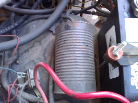 1981 Ford Bronco - A close-up view of a vehicle's engine bay reveals a battery and a cylindrical canister among various wires and hoses.
