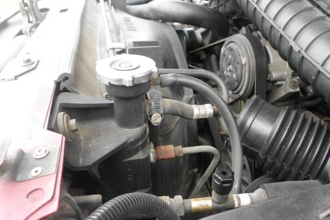 1994 Ford Bronco - Close-up view of engine bay components, including radiator cap and hoses, with a red fender on the left side.