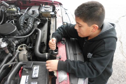 1994 Ford Bronco - A young person is focused on working on the engine of a vehicle, using a wrench on a hose clamp.