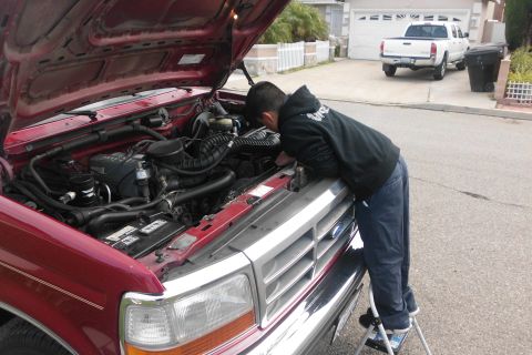 1994 Ford Bronco - A person inspects the engine of a 1994 Ford Bronco, which is parked in a driveway.