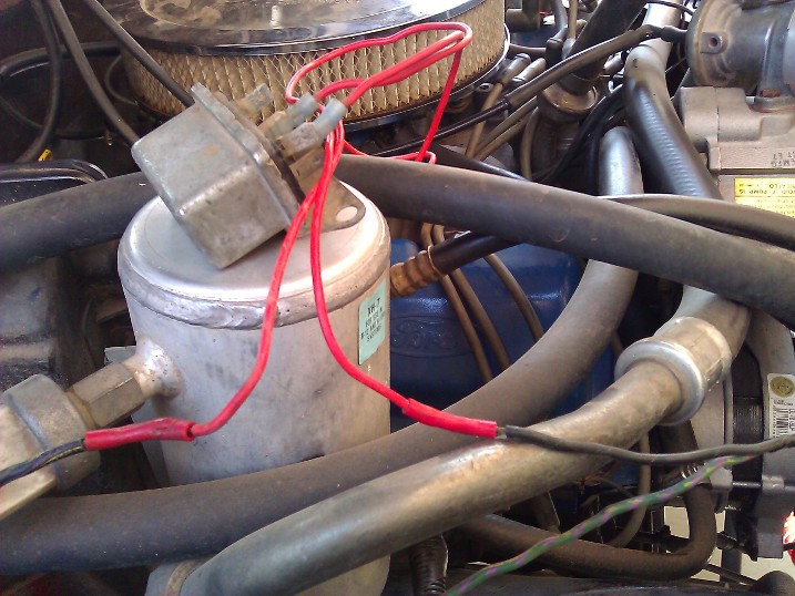 Engine bay with a small electrical box connected by red wires to AC components
