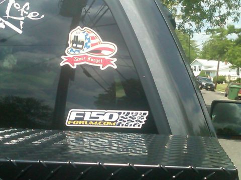 2008 Ford F-150 - Stickers on the rear window of a truck include F150Forum.com and a firefighter helmet with 'Never Forget'.