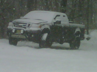 2008 Ford F-150 - A dark pickup truck is parked in a snowy environment, partially covered in snow.