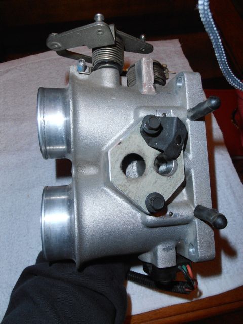 1990 Ford Bronco - A throttle body part is shown from a side angle, held by a gloved hand.