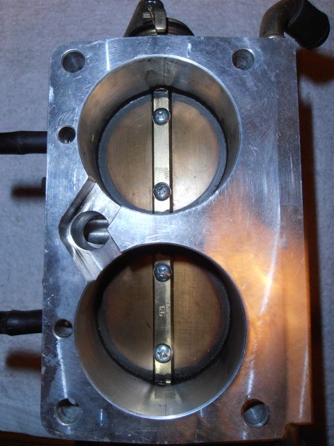 1990 Ford Bronco - A dual throttle body part with visible brass plates and screws, connected to black hoses.