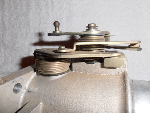 1990 Ford Bronco - Side closeup of a carburetor throttle linkage and lever mechanism mounted on a cast aluminum housing.