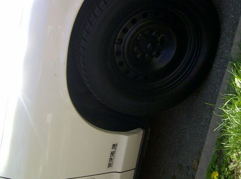 2000 Ford Crown Victoria - Close-up of a white car's fender and wheel, with a sticker visible on the lower body panel.