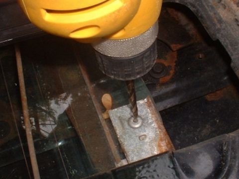1986 Ford Bronco - A drill bit is shown in action, working on a corroded metal bracket within a vehicle's interior.