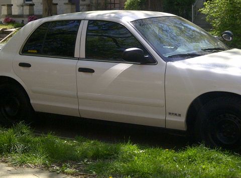 2000 Ford Crown Victoria - A white sedan is parked on a grassy area next to a sidewalk.