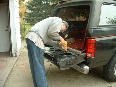 1986 Ford Bronco - A person is using a drill on the open tailgate of a vehicle, with tools and parts visible inside.