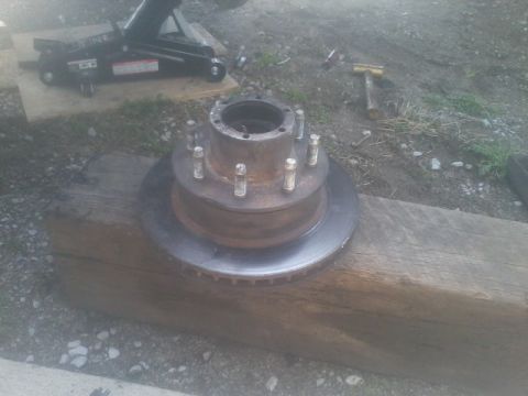 1995 Ford Bronco - A wheel hub and brake rotor assembly sits on a wooden beam, with a car jack and hammer visible in the background.