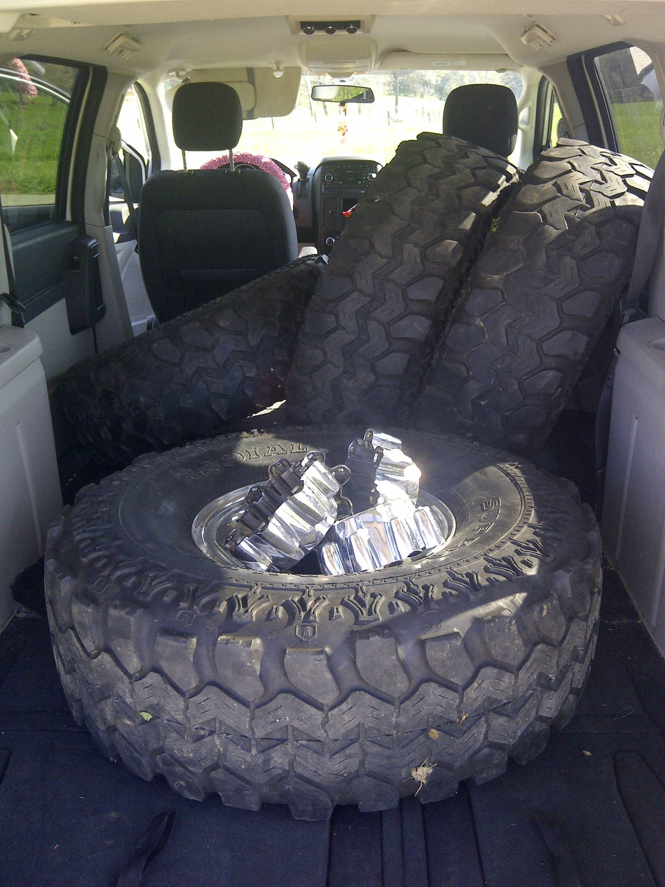 Several large off-road tires and chrome lug nuts piled in the back of a vehicle