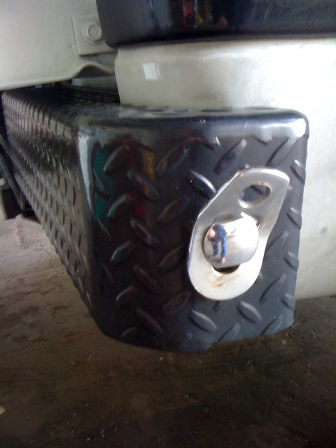 1997 Dodge 3500 - Close-up view of a vehicle's rear bumper corner, showing a black diamond plate texture and a chrome tie-down loop.