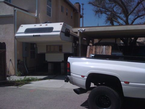 1997 Dodge 3500 - A white Dodge Ram pickup truck is parked next to a house, with a camper mounted in its bed.