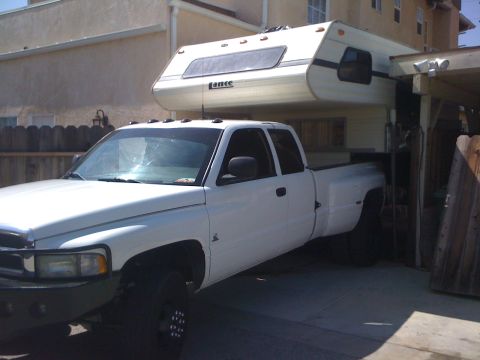 1997 Dodge 3500 - A white 1994 Dodge Ram 3500 dually pickup truck is equipped with a Lance camper shell and parked in a driveway.