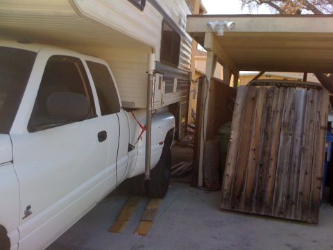1997 Dodge 3500 - A white pickup truck is parked under a carport, fitted with a camper shell and supported by wooden blocks.