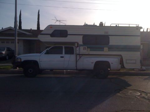 1997 Dodge 3500 - A white Dodge Ram pickup truck is outfitted with a large camper shell, parked on a residential street.