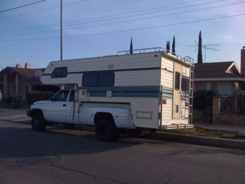 1997 Dodge 3500 - A white pickup truck with a camper shell is parked on the side of a street in front of houses.