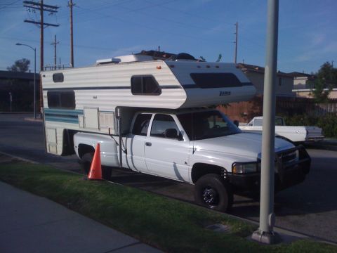 1997 Dodge 3500 - A white pickup truck is equipped with a camper shell, parked curbside with a traffic cone in front of the rear wheel.