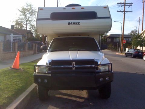 1997 Dodge 3500 - A white Dodge Ram pickup truck, likely from the mid-1990s, is parked curbside with a Lance camper mounted on its bed.