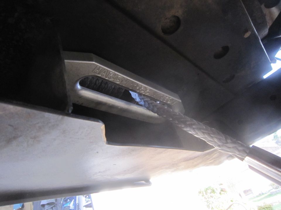 Close-up of a metal winch shackle mount with a braided rope attached, bolted to the underside of a vehicle