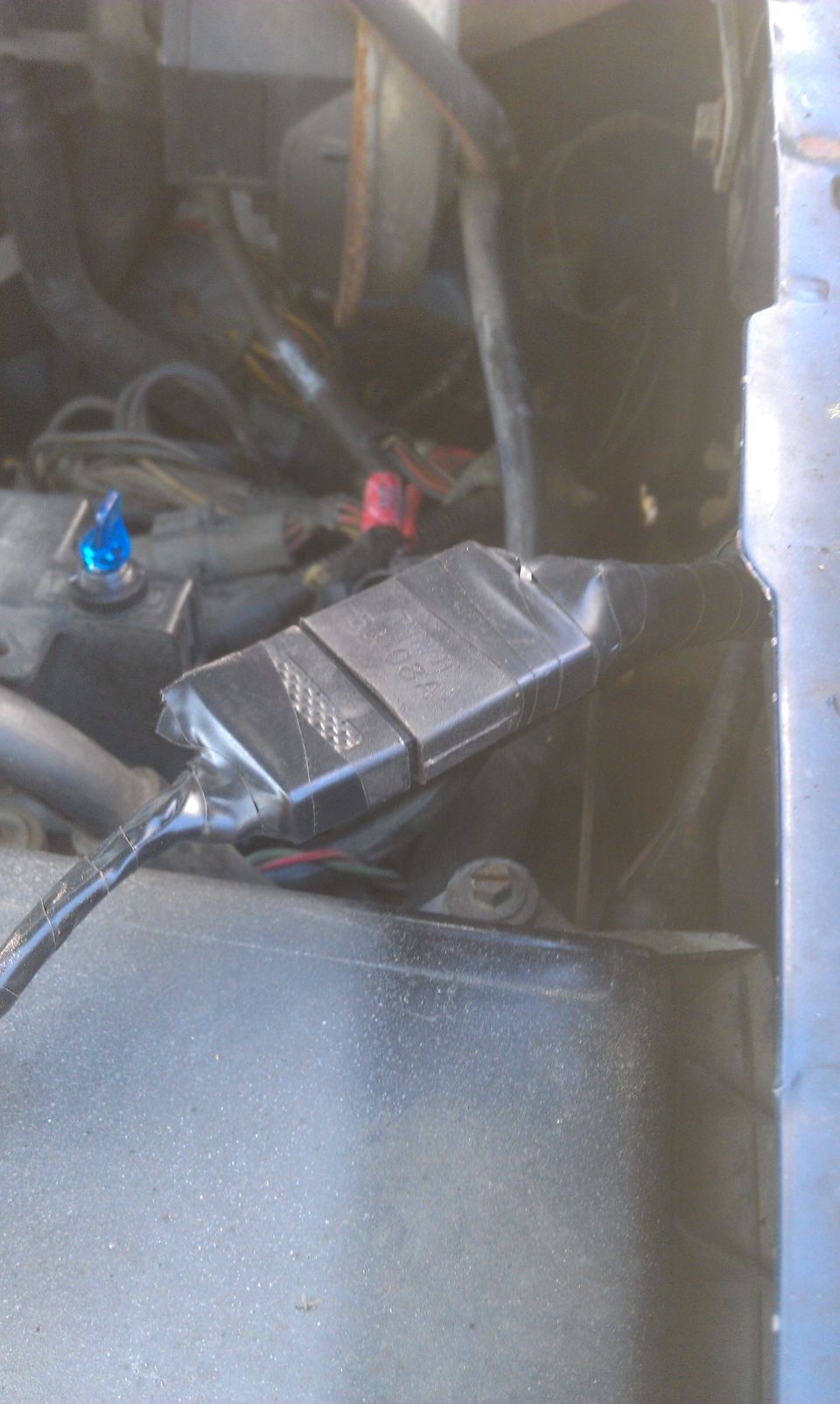 Engine bay wiring harness with a black plastic connector taped up. Blue indicator light visible