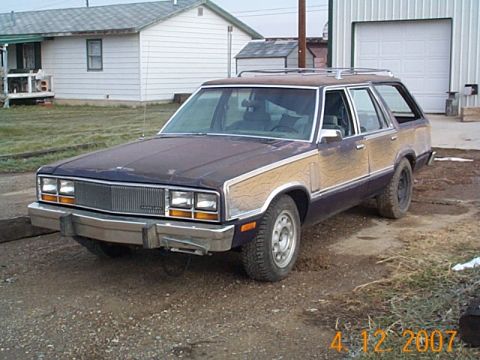 1982 Mercury Zephyr - Station wagon with woodgrain trim parked outside a garage and house.