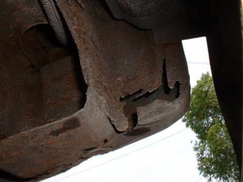 1986 Ford Bronco - Close-up view of a heavily rusted vehicle frame section, showing significant deterioration and a conduit pipe.