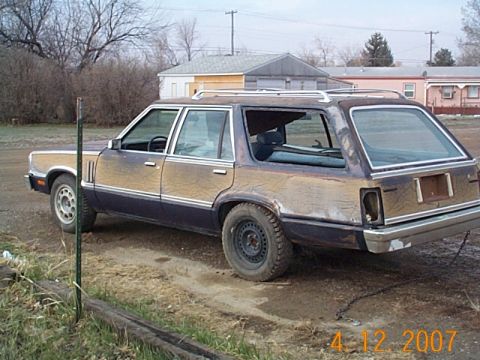 1982 Mercury Zephyr - A weathered station wagon sits in a dirt lot with buildings in the background.