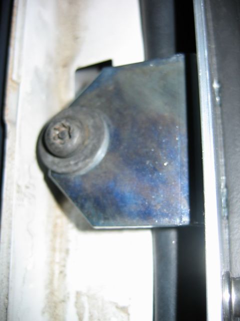 1992 Ford Bronco - Extreme close-up of a heat-blued steel door striker plate with a rounded torx-head striker bolt, mounted to a body pillar beside black weat…