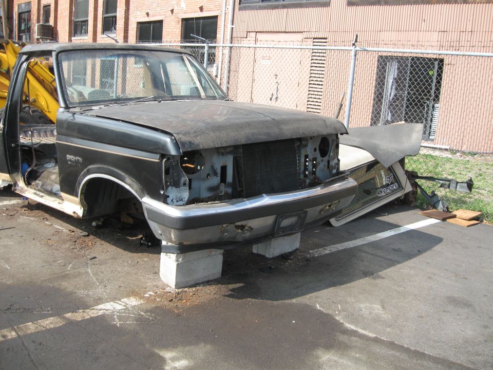 Black Ford F-Series truck, front end damaged, supported by concrete blocks