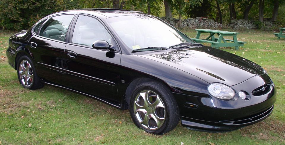 Black Ford Taurus sedan with chrome multi-spoke wheels parked on grass near picnic tables