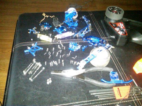 1986 Ford Bronco - Various blue aluminum parts and tools, including pliers and a remote control transmitter, are laid out on a dark surface.