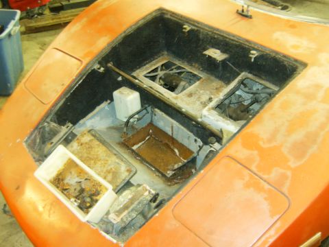 2000 Ford E350 - The open engine bay of an orange car shows signs of disrepair and rust, with debris collected in a white container.