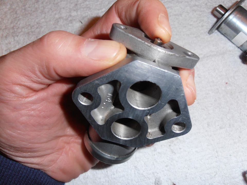 Metal automotive part held in hand, showing multiple circular openings and internal passages