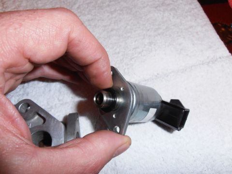 1990 Ford Bronco - A hand holds an idle air control valve, a component used in vehicle emissions control systems.