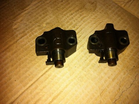 1998 Ford Crown Victoria - Two engine timing chain tensioners are shown resting on a wooden surface.