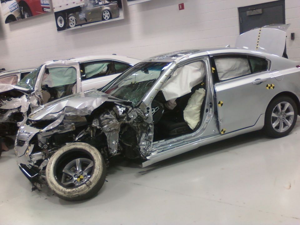 Silver sedan with deployed airbags and heavy front-end damage, parked next to another damaged car