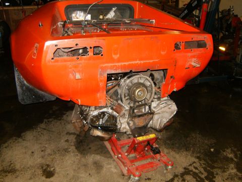 2000 Ford E350 - The rear of an orange sports car is shown with its engine and drivetrain exposed, supported by a red jack.