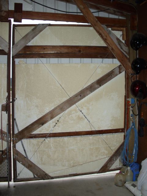 1989 Ford Bronco - The interior of a barn shows a large, rustic wooden door with diagonal bracing and some hanging helmets on the right side.