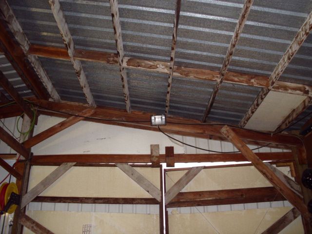View of a barn's corrugated metal roof and wooden beams. A light fixture is mounted on a beam