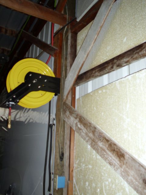 1989 Ford Bronco - A yellow hose reel is mounted on a black bracket in a workshop setting.