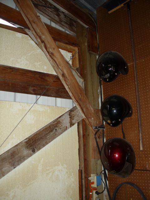 1989 Ford Bronco - Three helmets, two black and one red, hang from a hook on a pegboard wall in a garage.